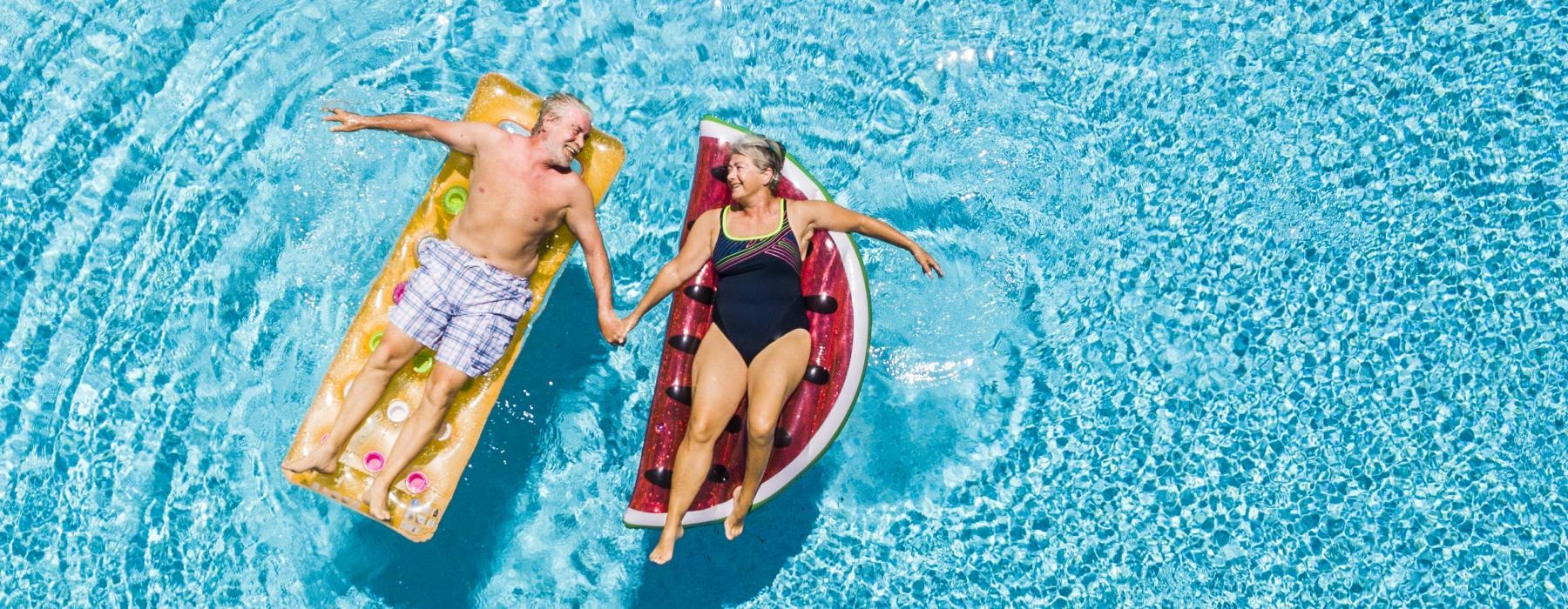 older couple laying on floaters in pool